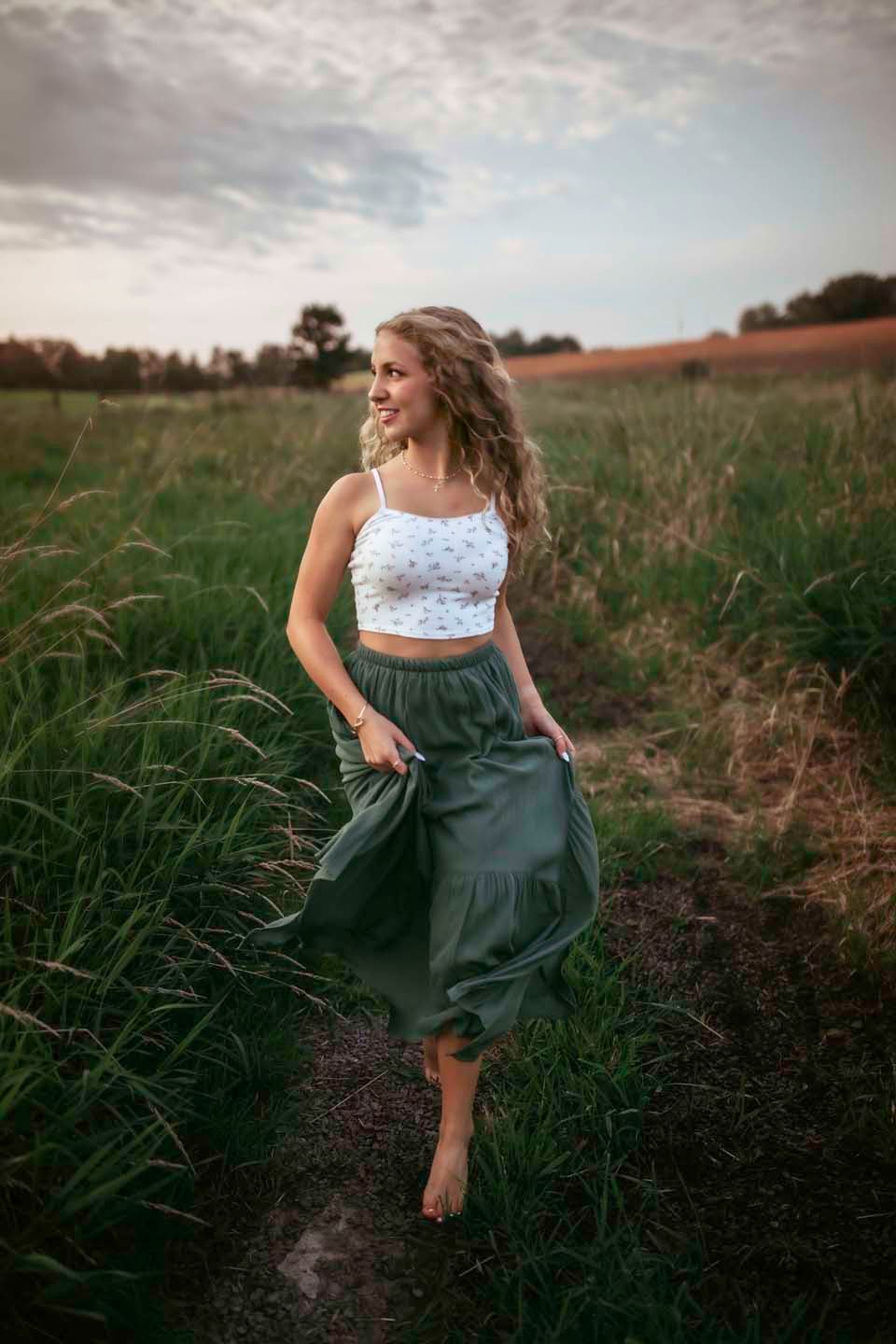 Barefoot dancing in flowing green skirt and lace crop top at sunset in rural field.