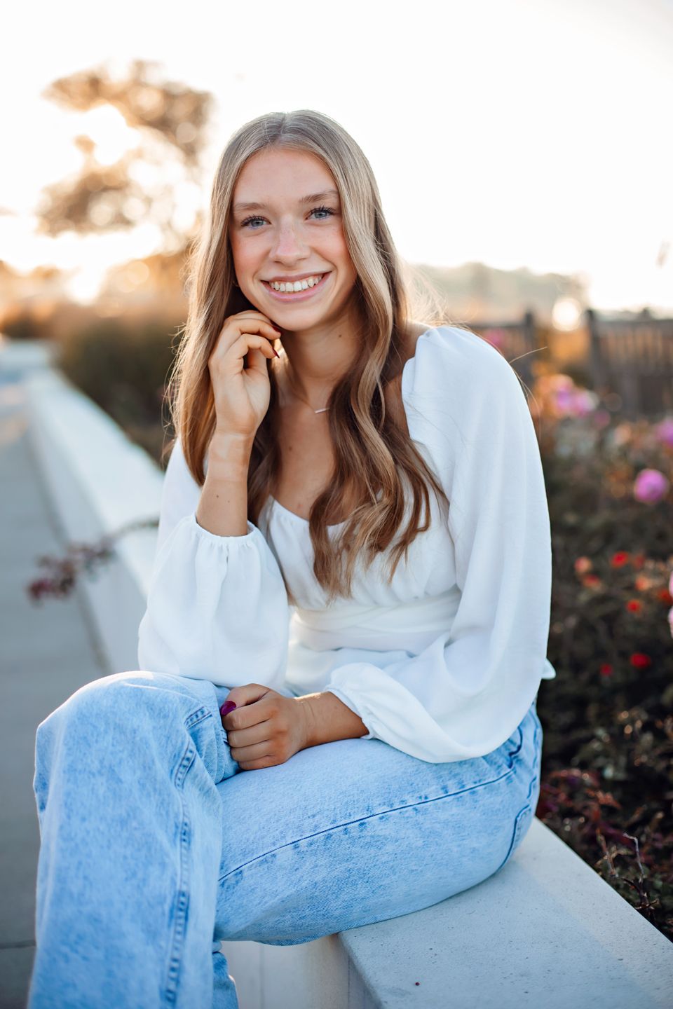Casual portrait of someone in a white sweater and jeans sitting outdoors at sunset.