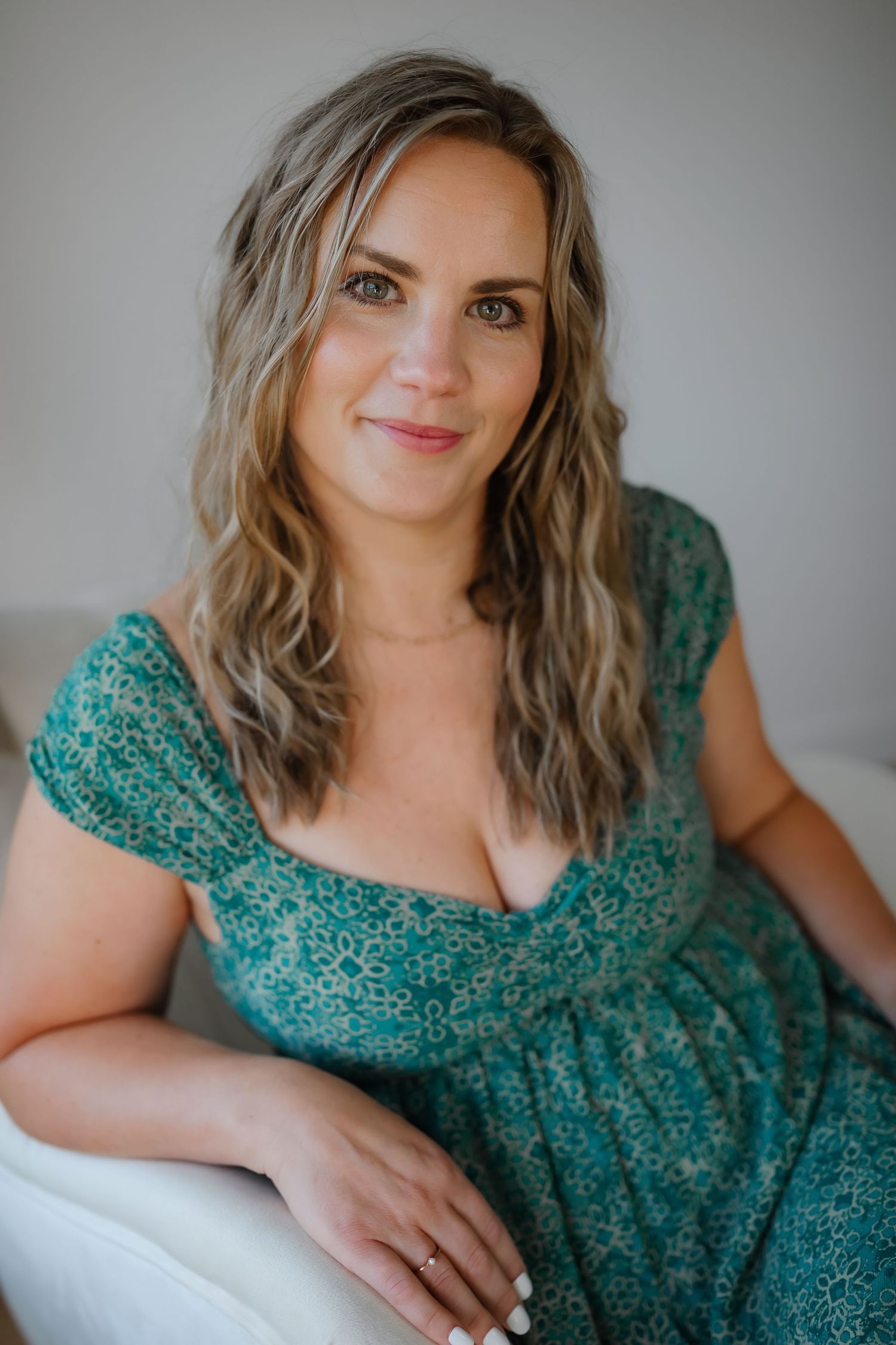 Indoor portrait wearing teal floral dress against neutral background.