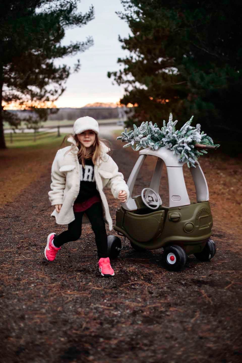 Child-sized toy car decorated with winter greenery on a rustic outdoor trail at sunset.