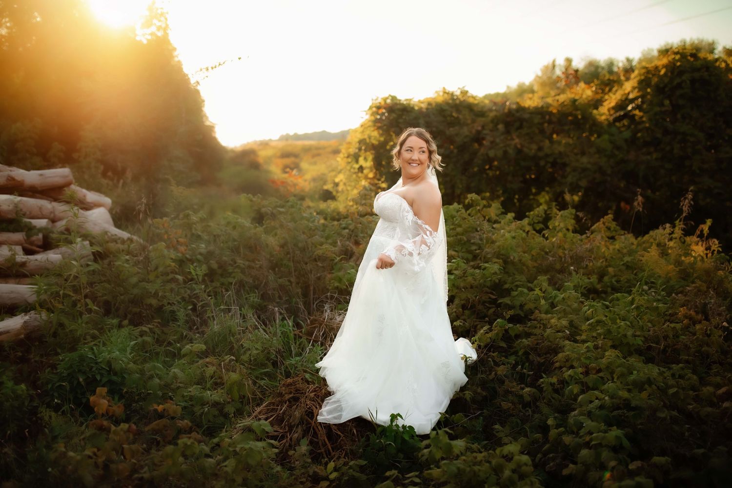 Bride in flowing white dress poses on hillside during golden hour sunset.