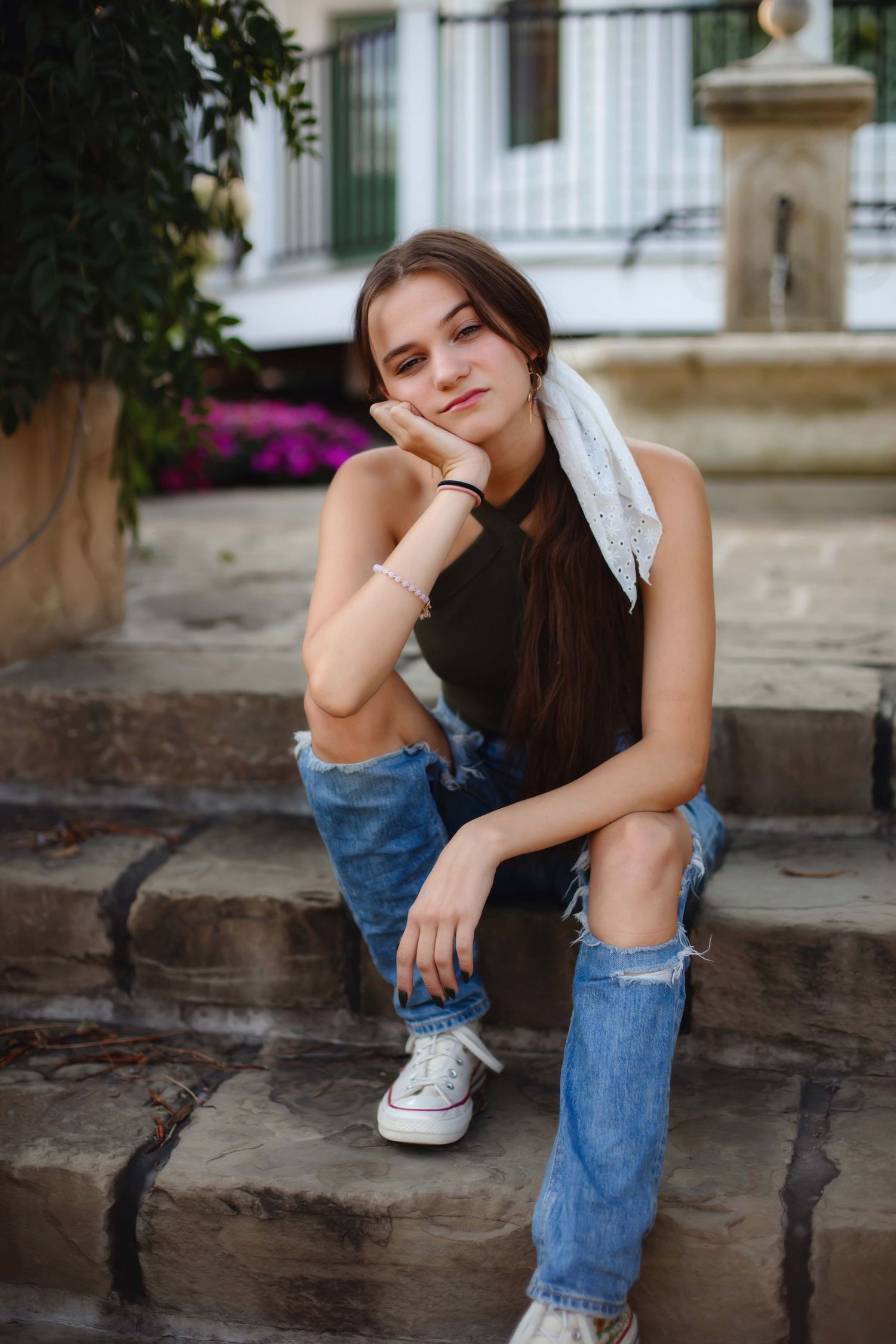 Person in casual denim and black top posing on stone steps near flowers.