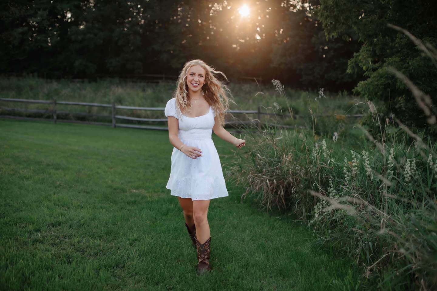 Dancing in white dress and boots on green grass at golden hour.