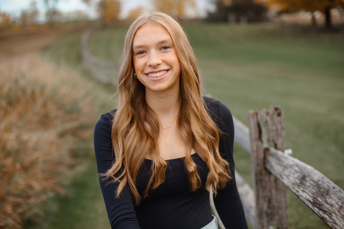 Outdoor autumn portrait showcasing long hair and a black sweater against a natural countryside backdrop.