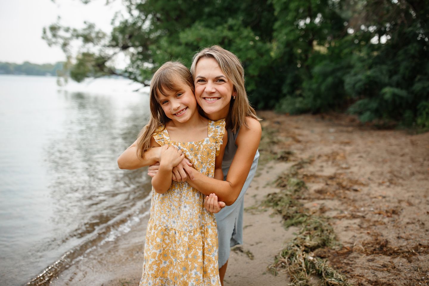 A joyful moment between two people embracing on a sandy beach by a calm lake on a summer evening.
