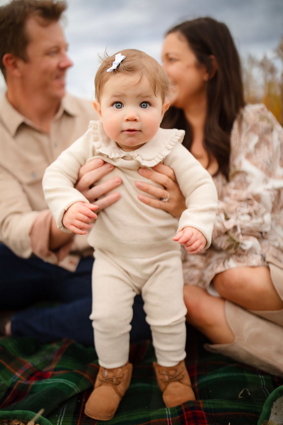 A sweet family moment captured on plaid blanket during outdoor photo session.