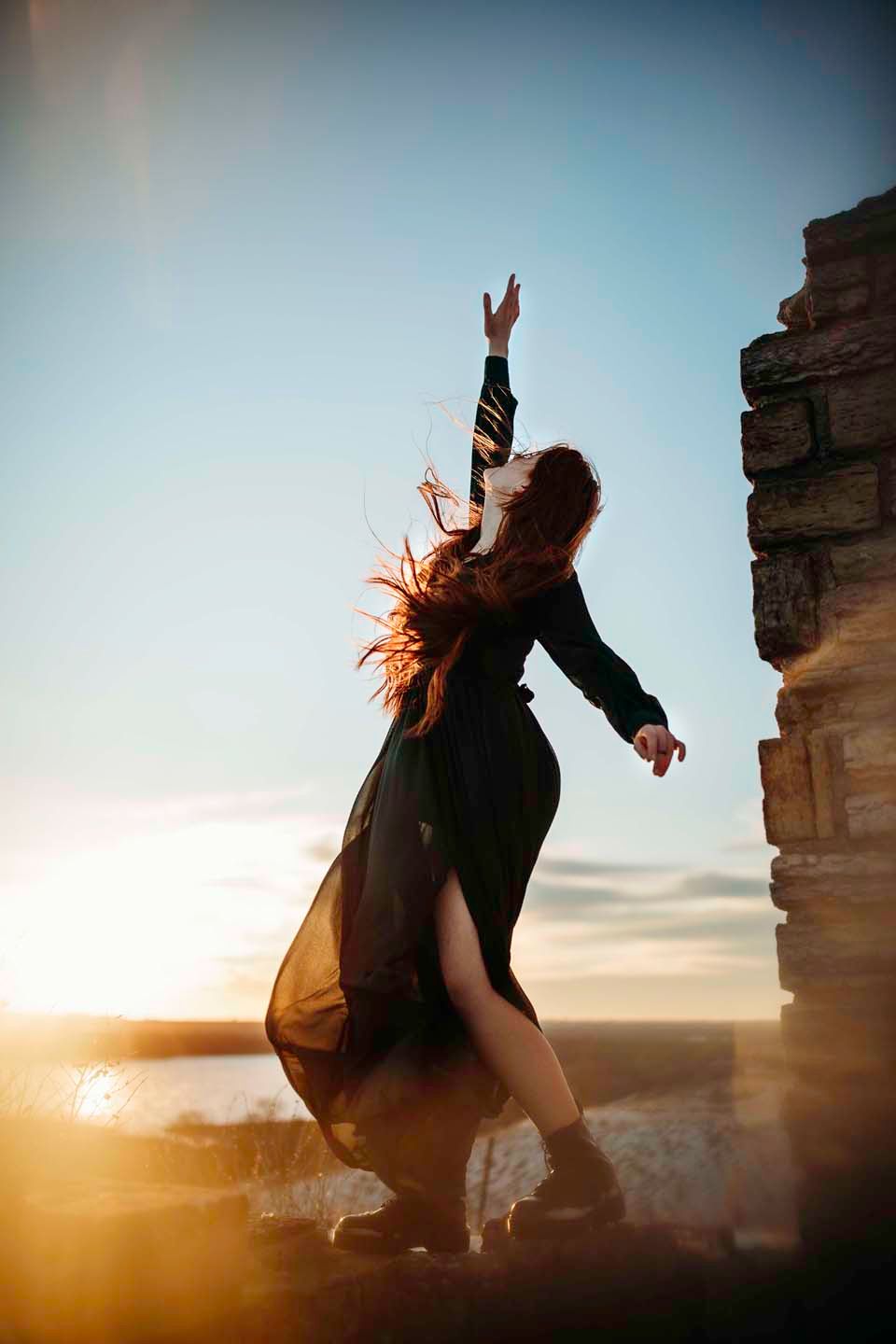 A silhouetted figure in flowing dress dances atop stone ruins at sunset.