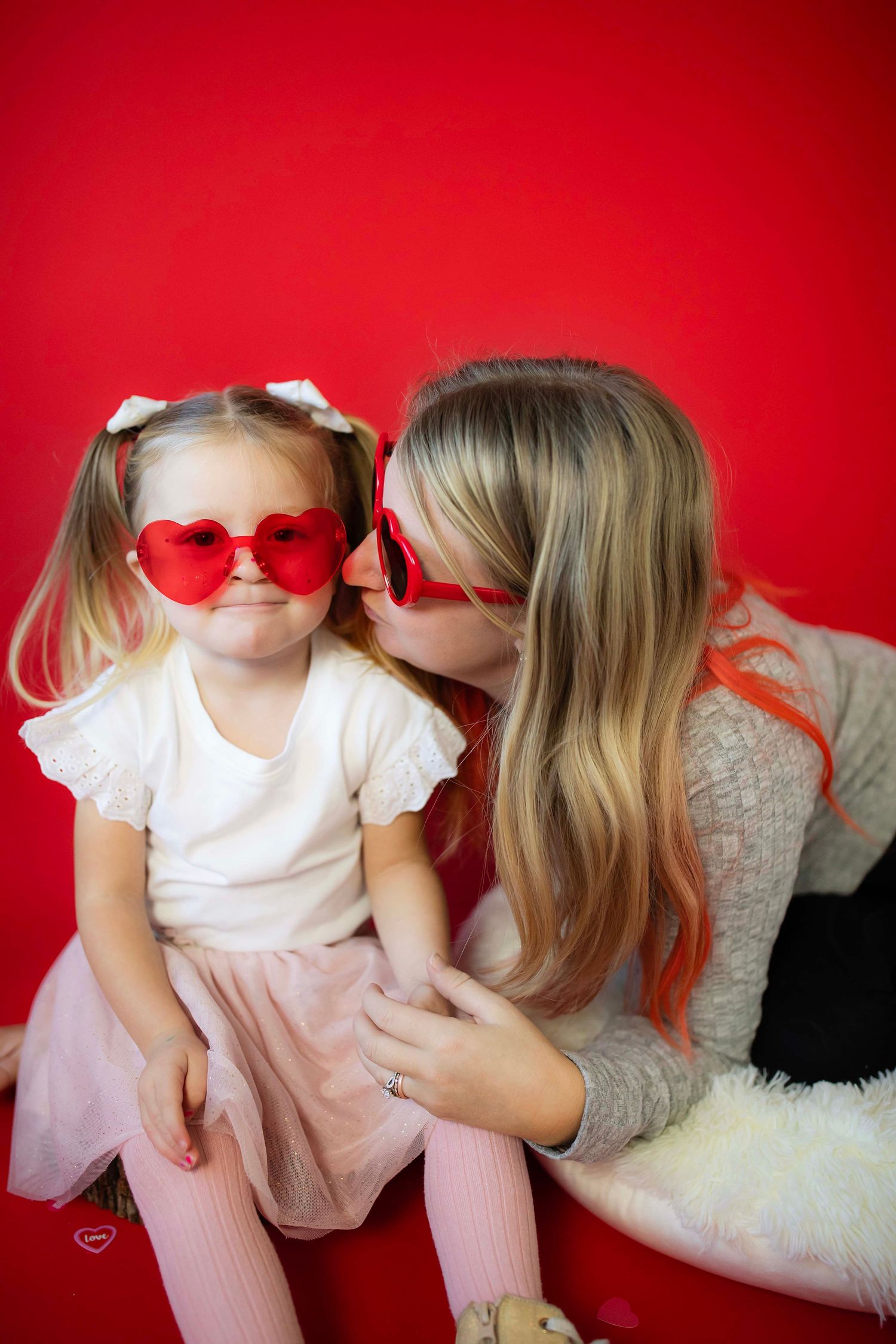 Sweet Valentine's Day themed portrait with matching heart sunglasses against red backdrop.