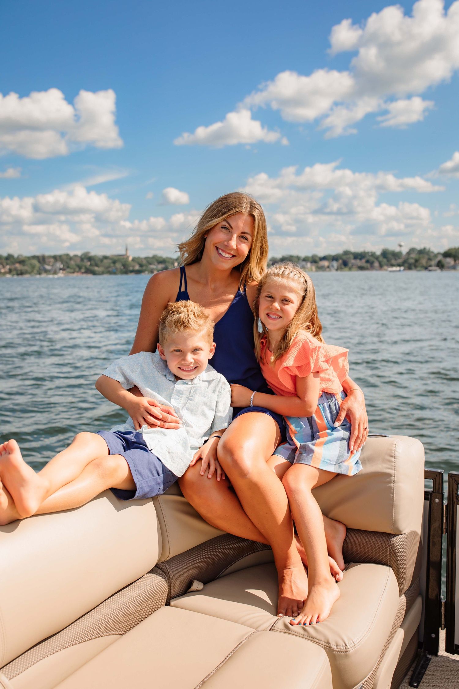 Cheerful family moment captured on a boat with sparkling water and puffy clouds in the background.
