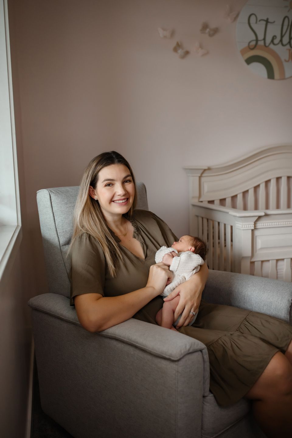 A tender moment in a nursery featuring a comfortable grey armchair and rainbow wall decor.