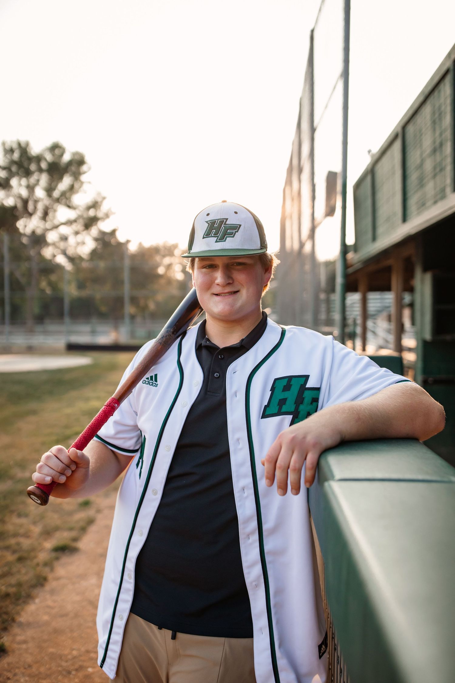 Baseball player holding bat against fence during golden hour.