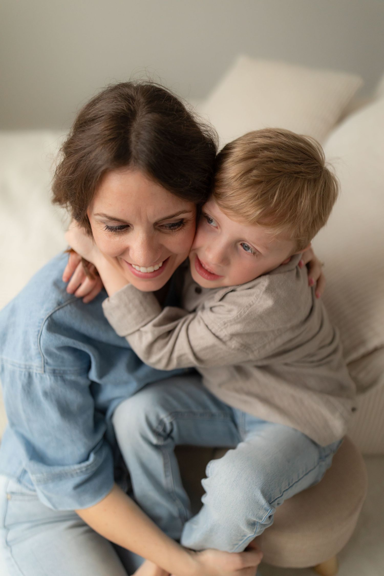 Mother and child share playful cuddles and laughter while sitting together in casual denim outfits.