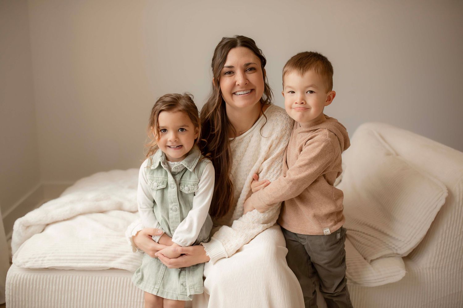 Family members share tender moments together while posing in soft neutral tones against a light beige backdrop.