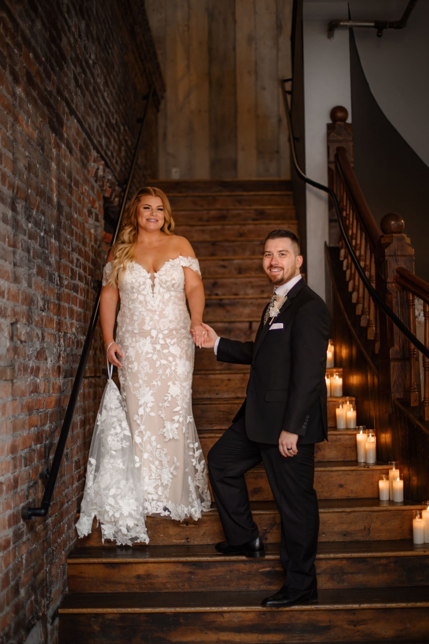 Elegant wedding portrait on vintage staircase with candlelight and exposed brick backdrop.