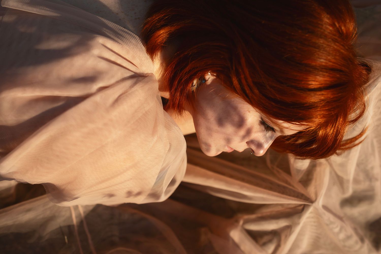 Dramatic portrait with flowing white fabric and red hair in soft lighting.