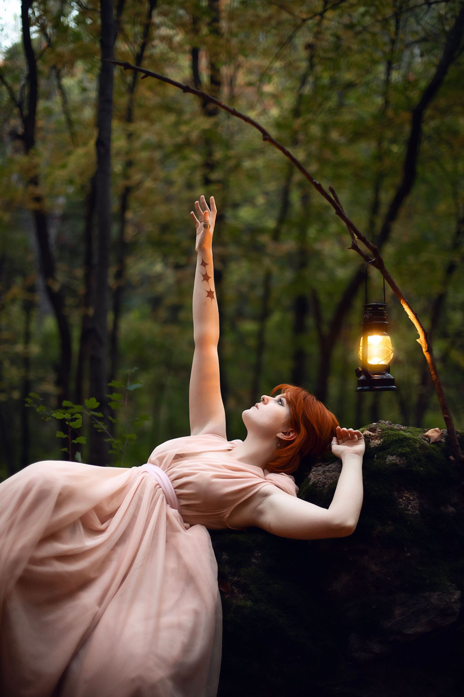 An ethereal pose on dark rocks with a lantern hanging nearby in a mystical forest setting.