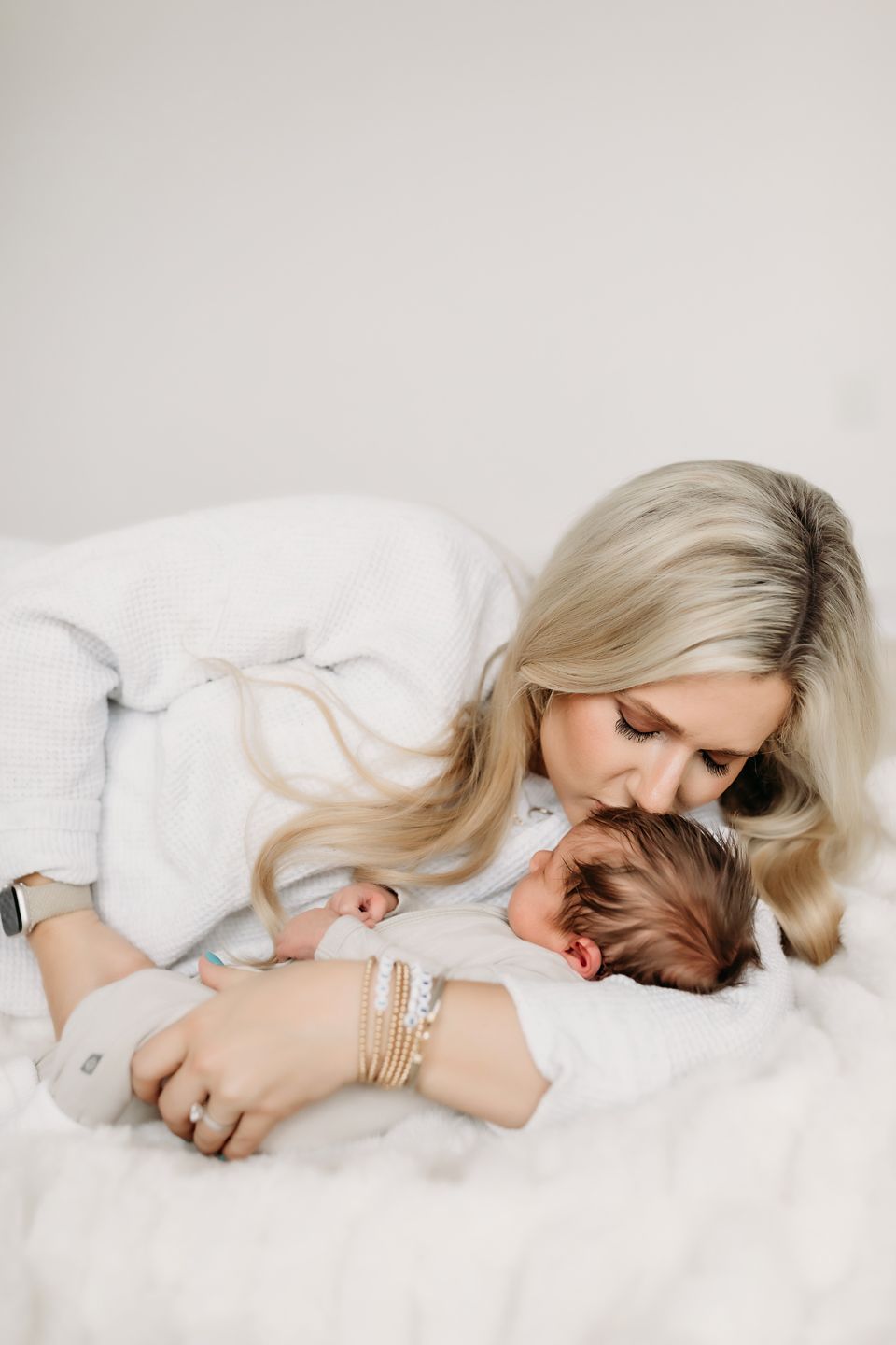 Intimate portrait of maternal embrace on white bedding.