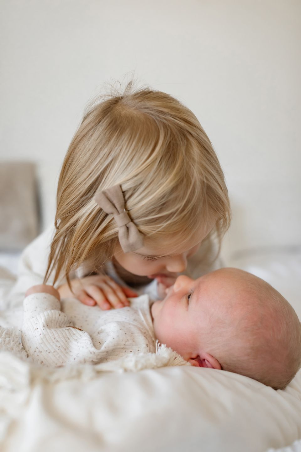 Gentle sibling moment with soft neutral tones on white bedding.