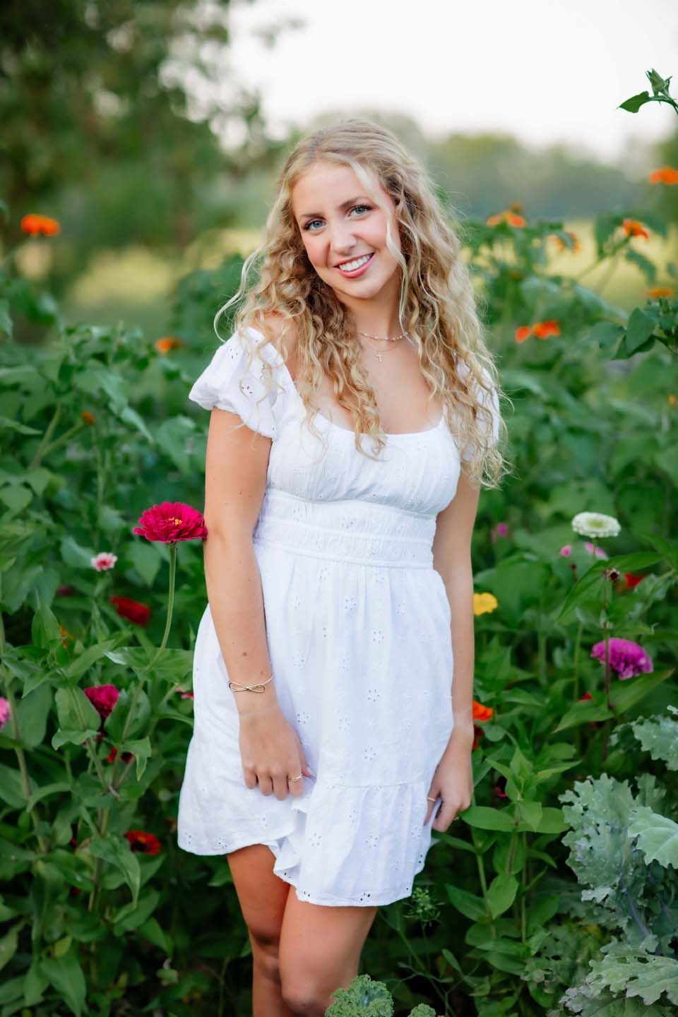 Summer garden portrait in white eyelet dress surrounded by colorful flowers.
