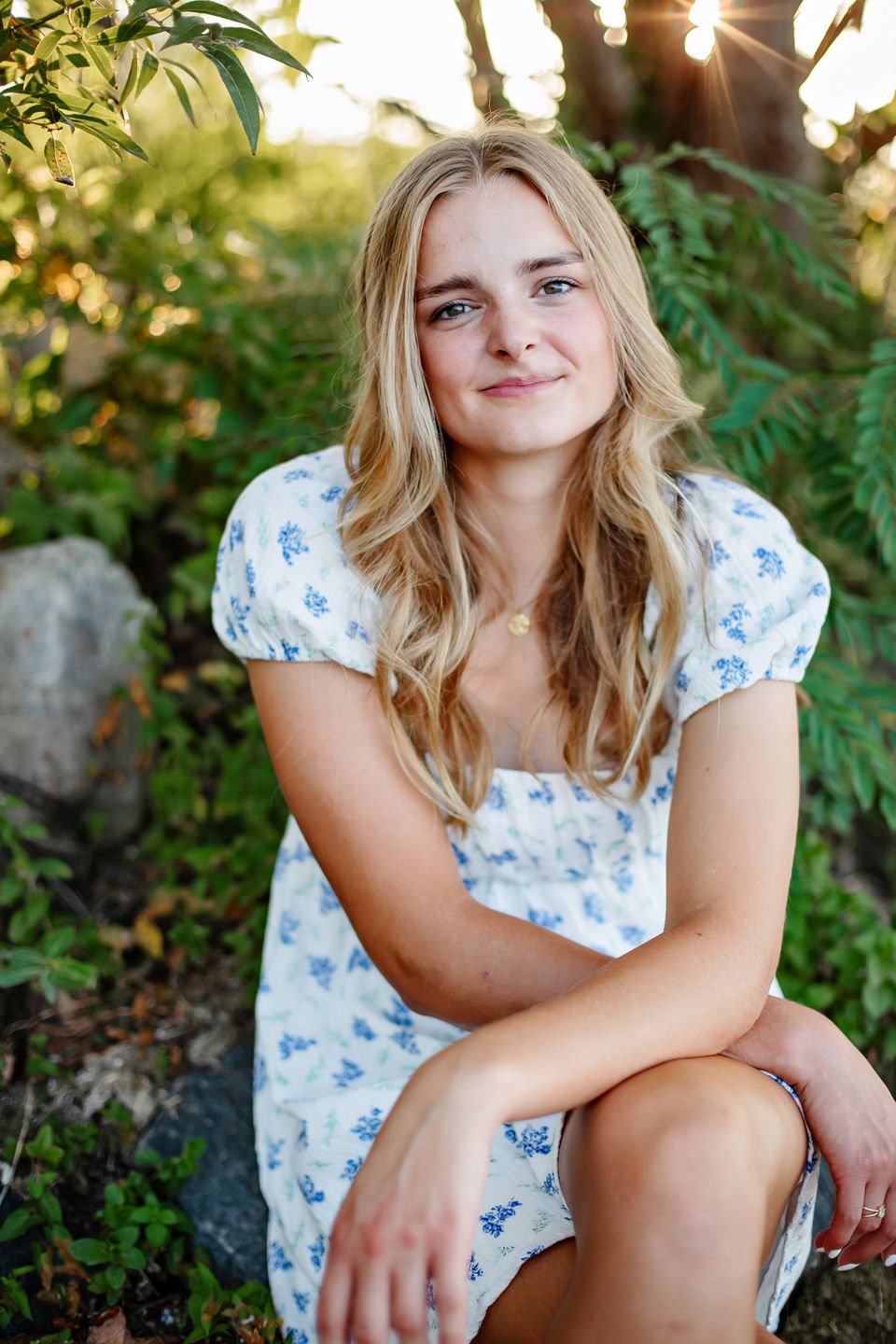 A summer portrait in a floral dress with sunlit trees and greenery in the background.