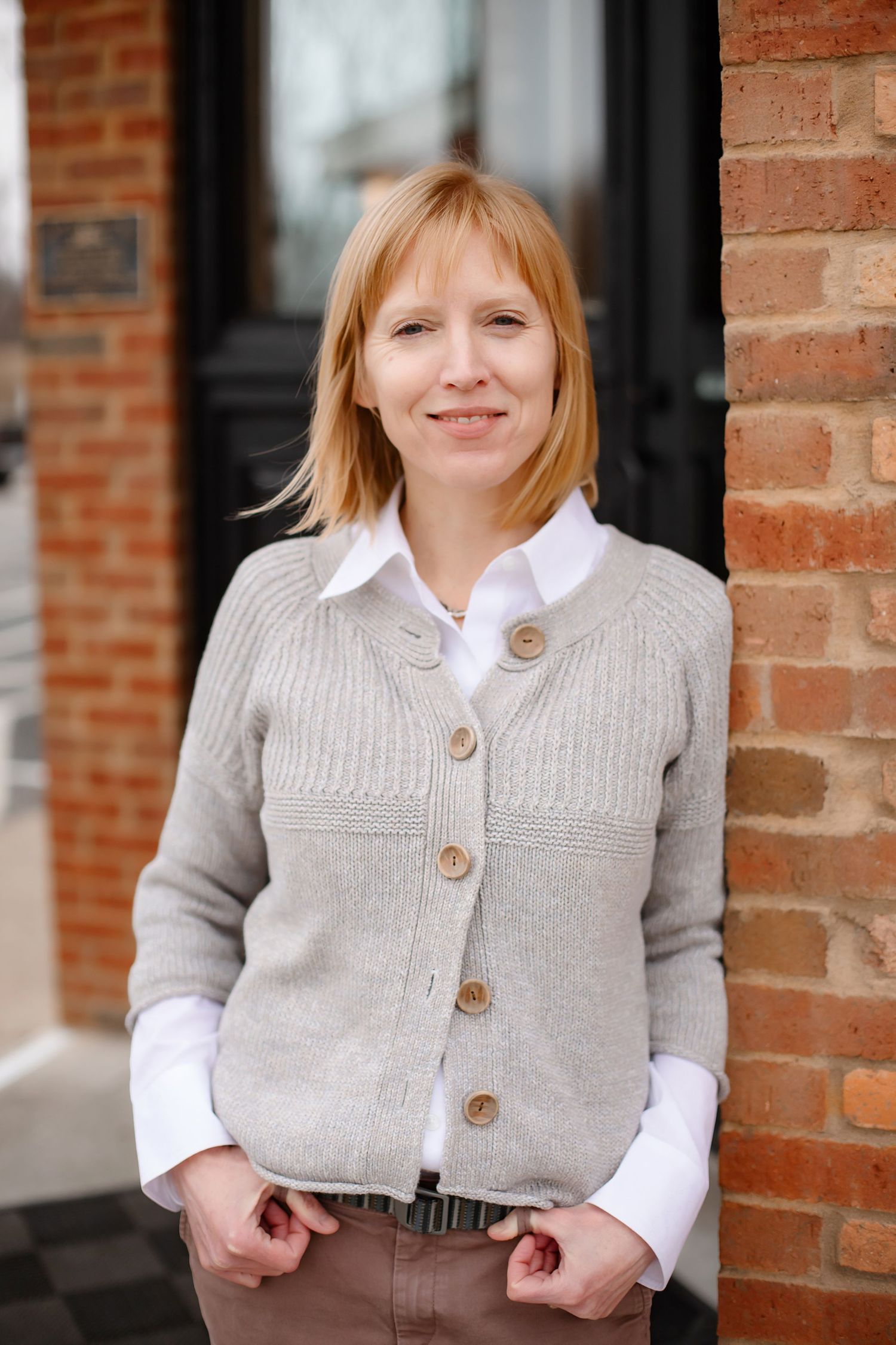 Professional portrait against brick wall wearing beige cardigan and white collared shirt.