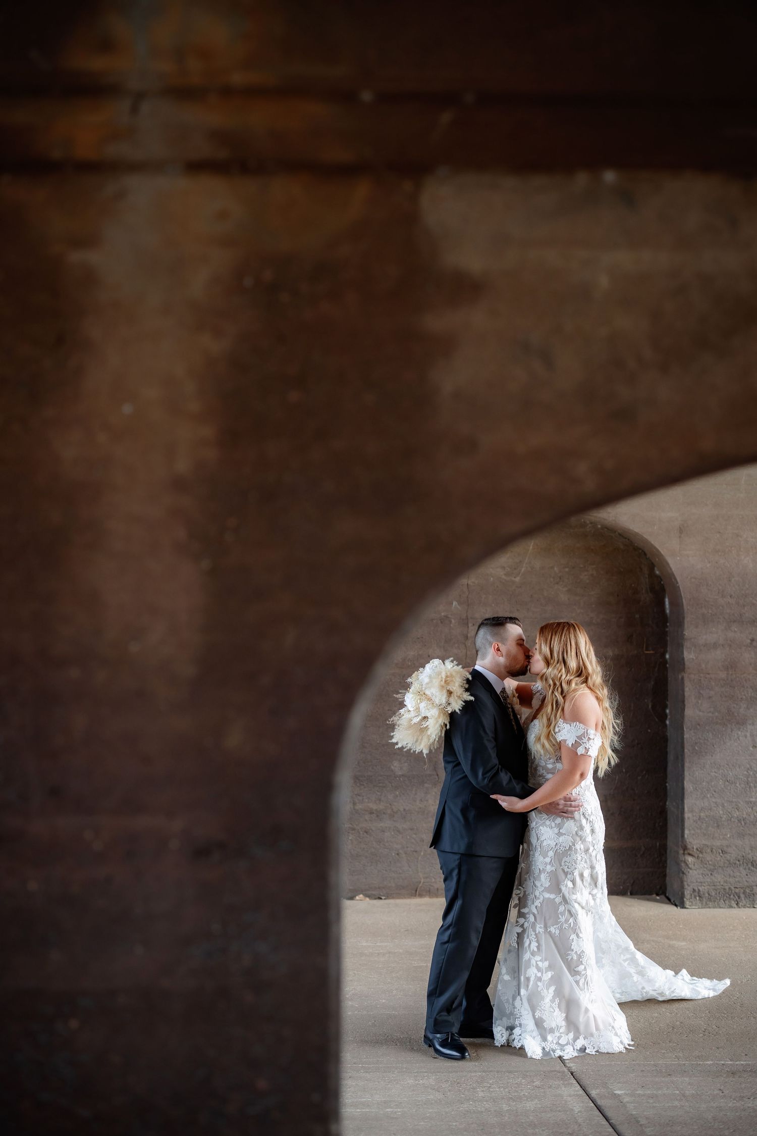 Romantic wedding couple shares an intimate moment under a stone archway with dramatic lighting.