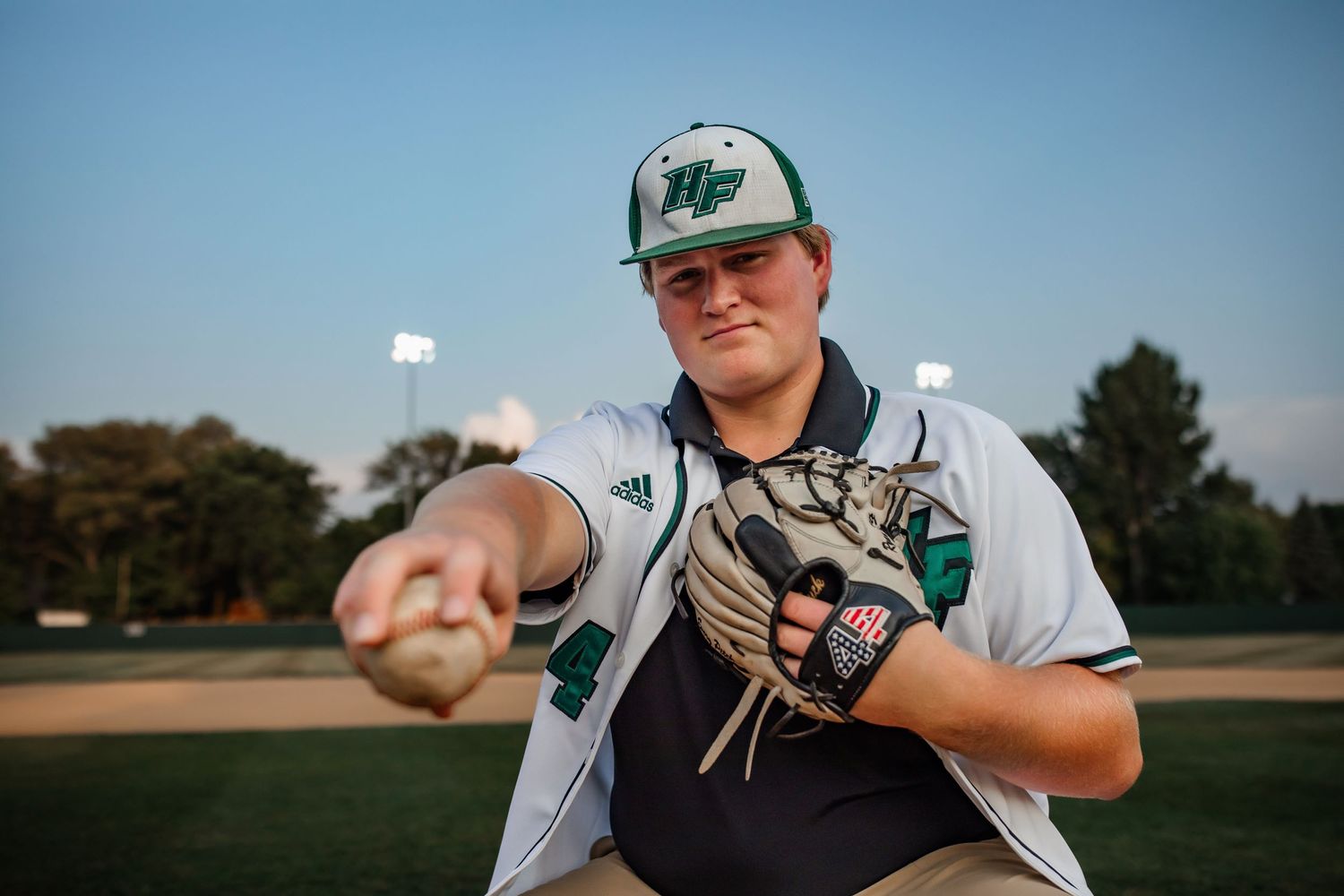 Baseball player in pitching stance demonstrates throwing form on baseball field at dusk.