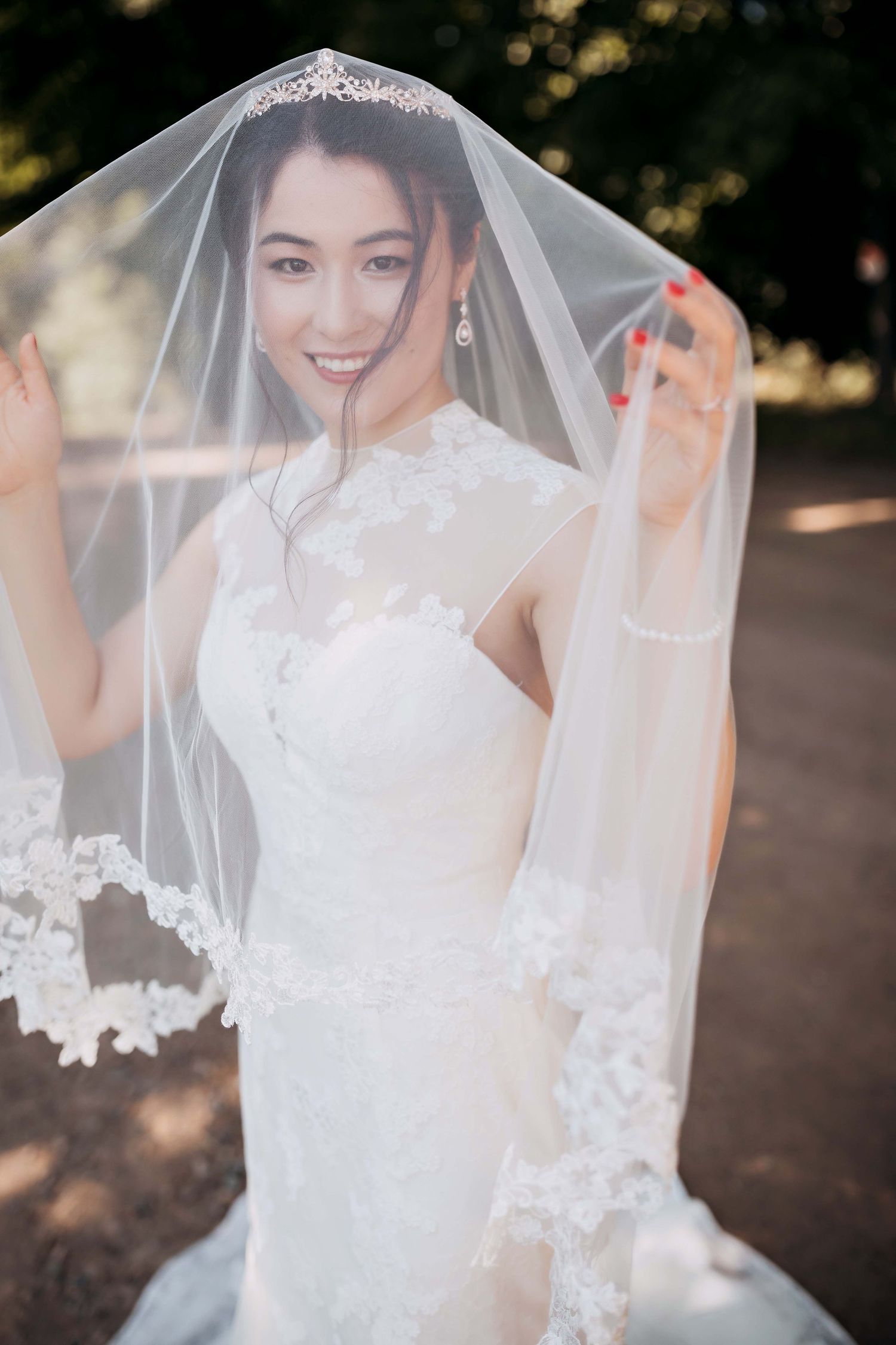 Elegant bride in lace wedding gown with detailed veil posing outdoors.