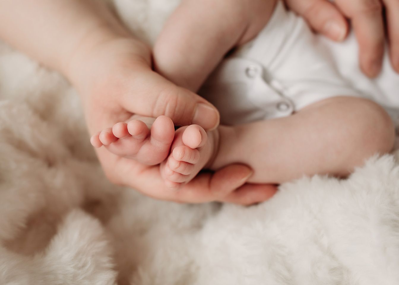 Close-up of tiny newborn feet being gently held in adult hands against soft fabric.