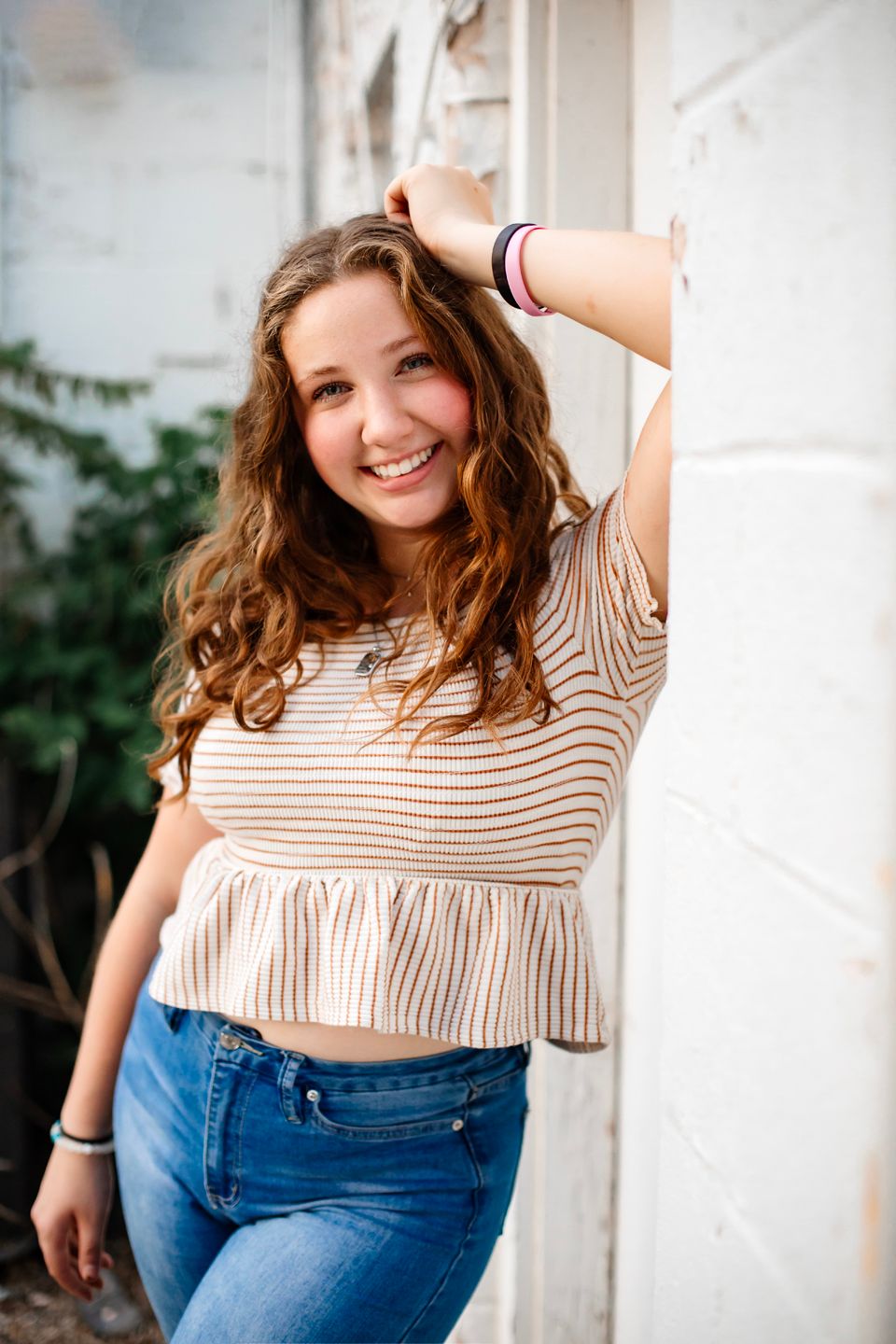 Person in striped top and jeans poses casually against white wall.