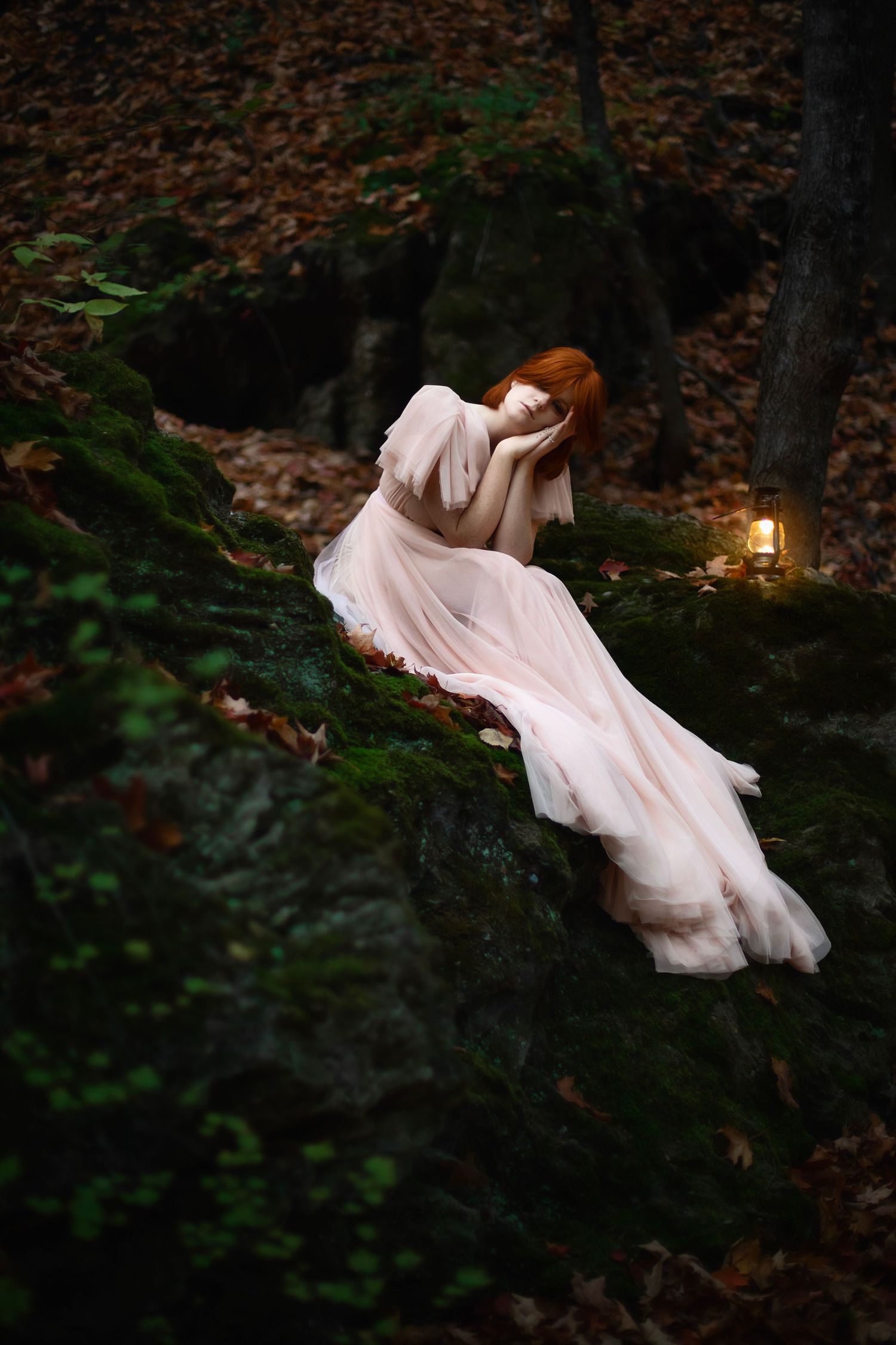 A dreamy photograph of a flowing pink dress against dark rocks with a lantern in a mystical forest.