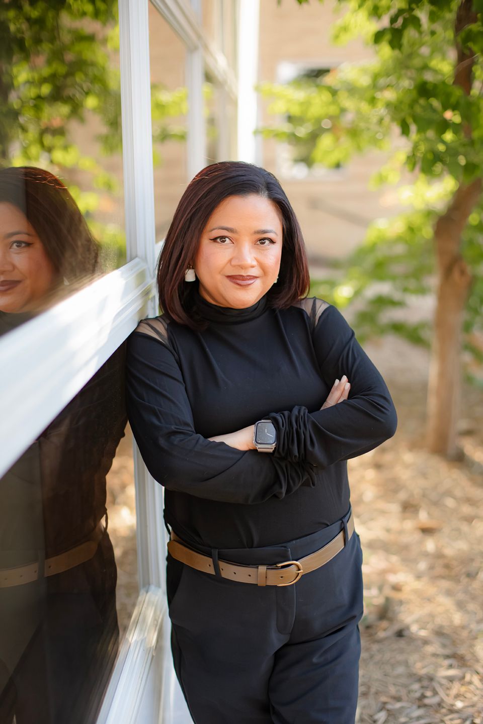 Professional wearing a black outfit and brown belt poses against a light background with trees in multiple angles.