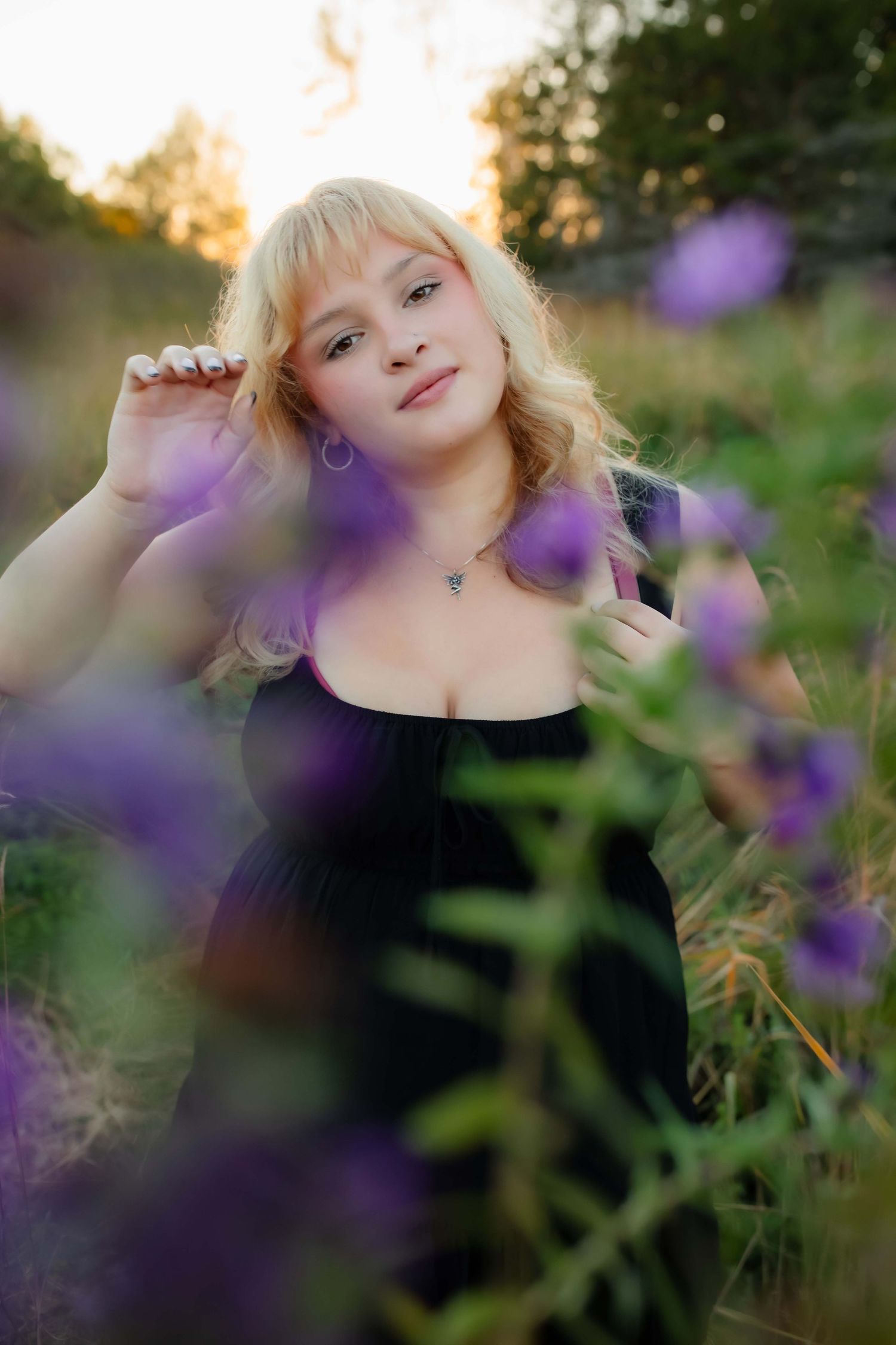 Artistic portrait through purple flowers with soft focus and warm sunset lighting in background.