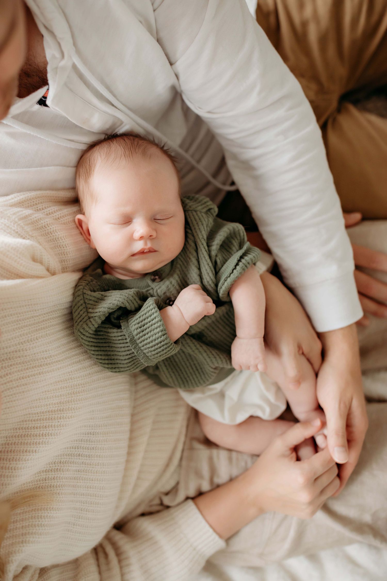 Sleeping infant in green knit outfit nestled against caregiver in white.