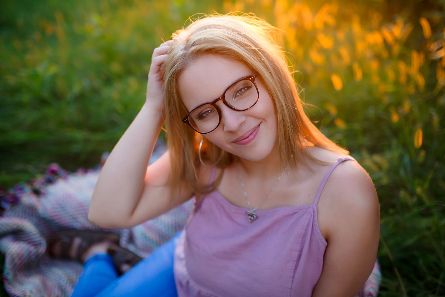 A dreamy portrait of someone wearing glasses and a purple tank top in golden hour lighting outdoors.