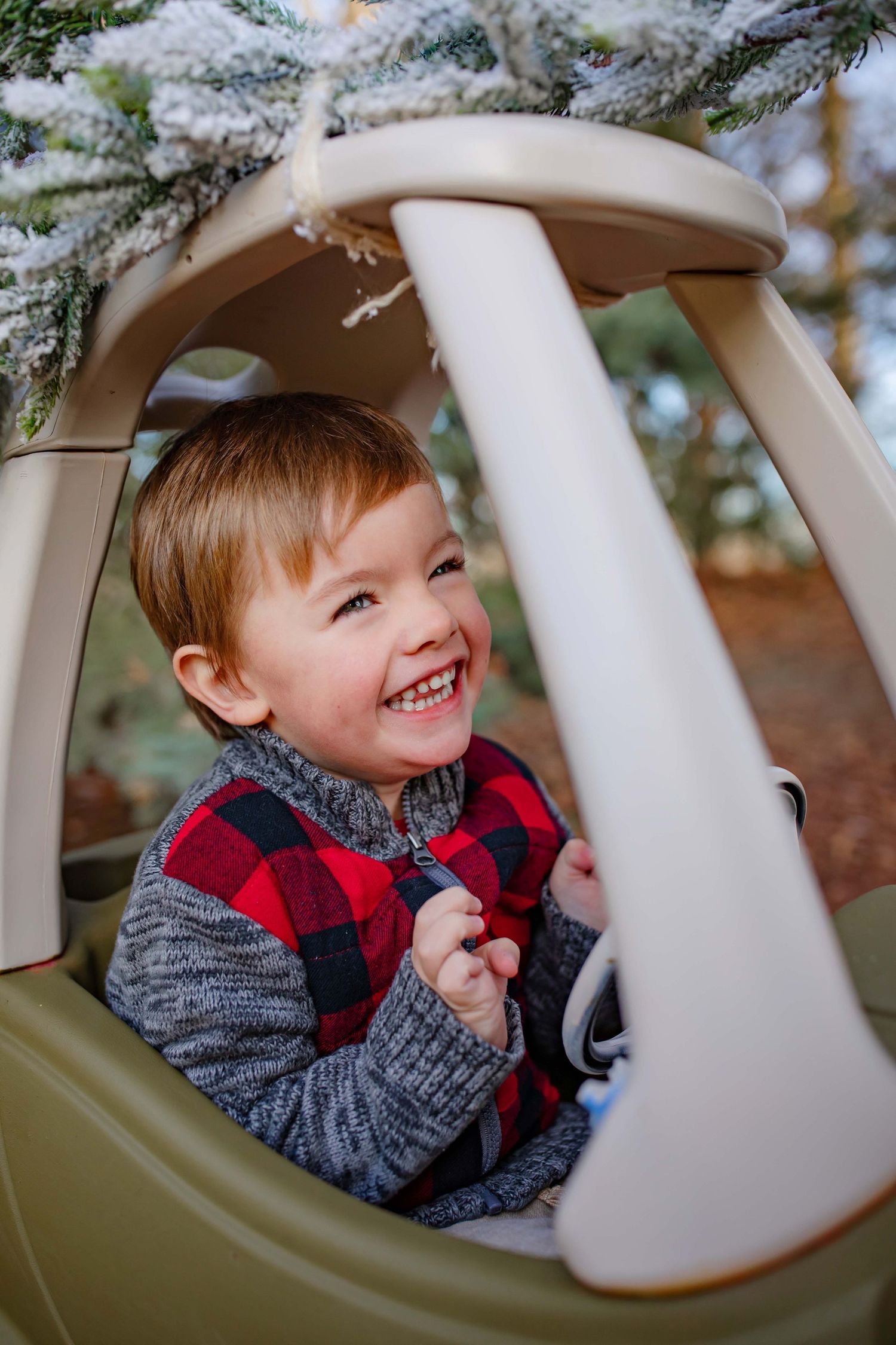 Child playing in toy coupe car decorated with holiday greenery in outdoor setting.