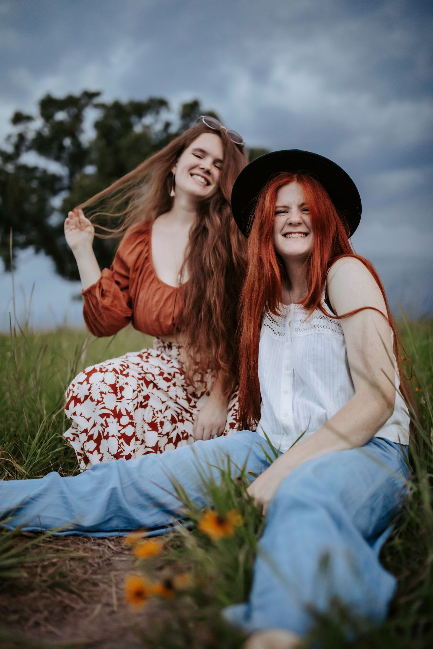 Friends laughing and sitting in a grassy field wearing contrasting casual outfits.