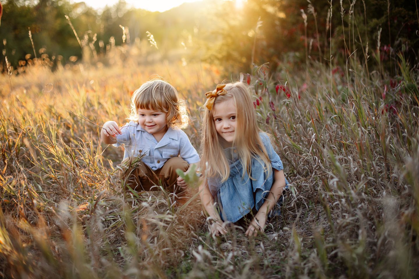 Two children explore a wildflower meadow together during golden hour as sunlight streams through the natural setting.