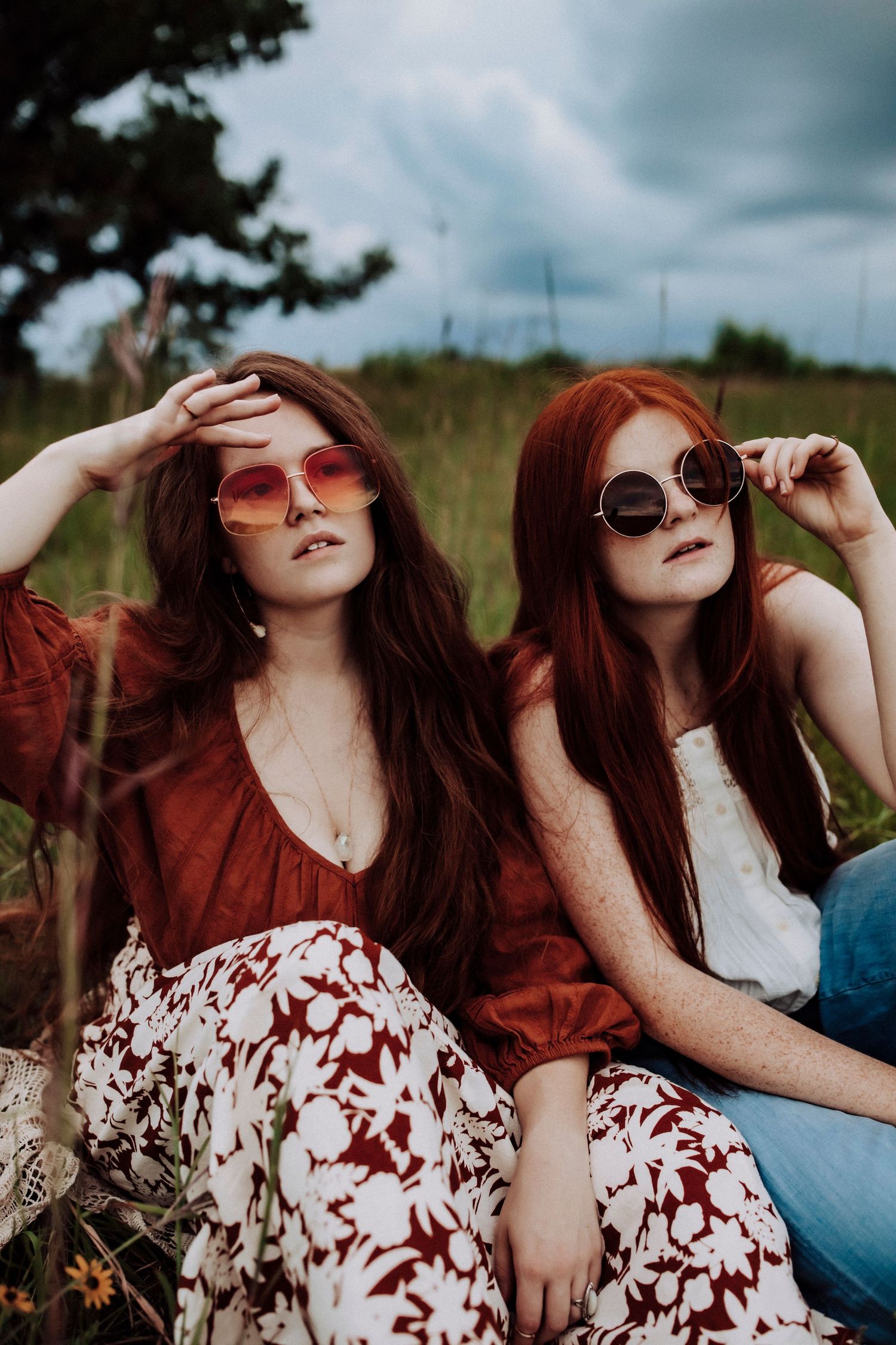 Two friends wearing sunglasses and red outfits pose together in a field on a cloudy day.