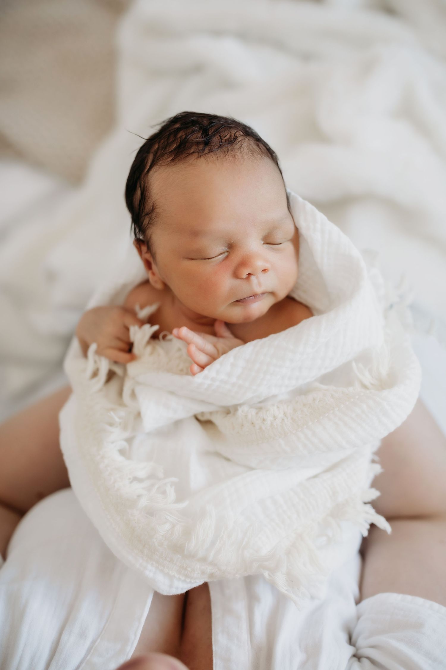Sleeping newborn baby swaddled in white textured blanket with soft lighting.