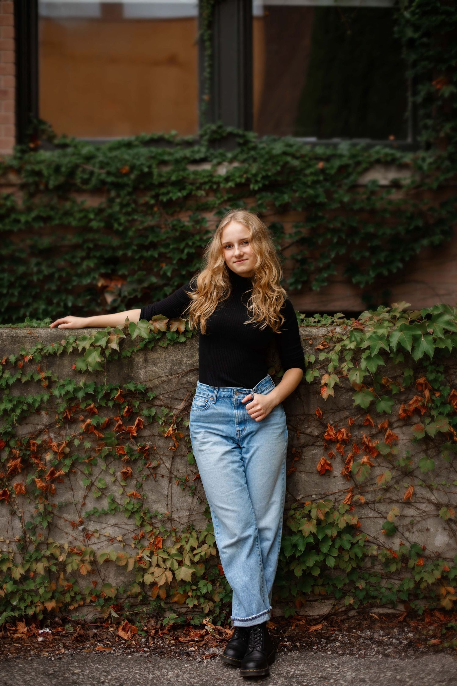 Casual autumn style portrait against brick wall with climbing ivy creating natural backdrop.