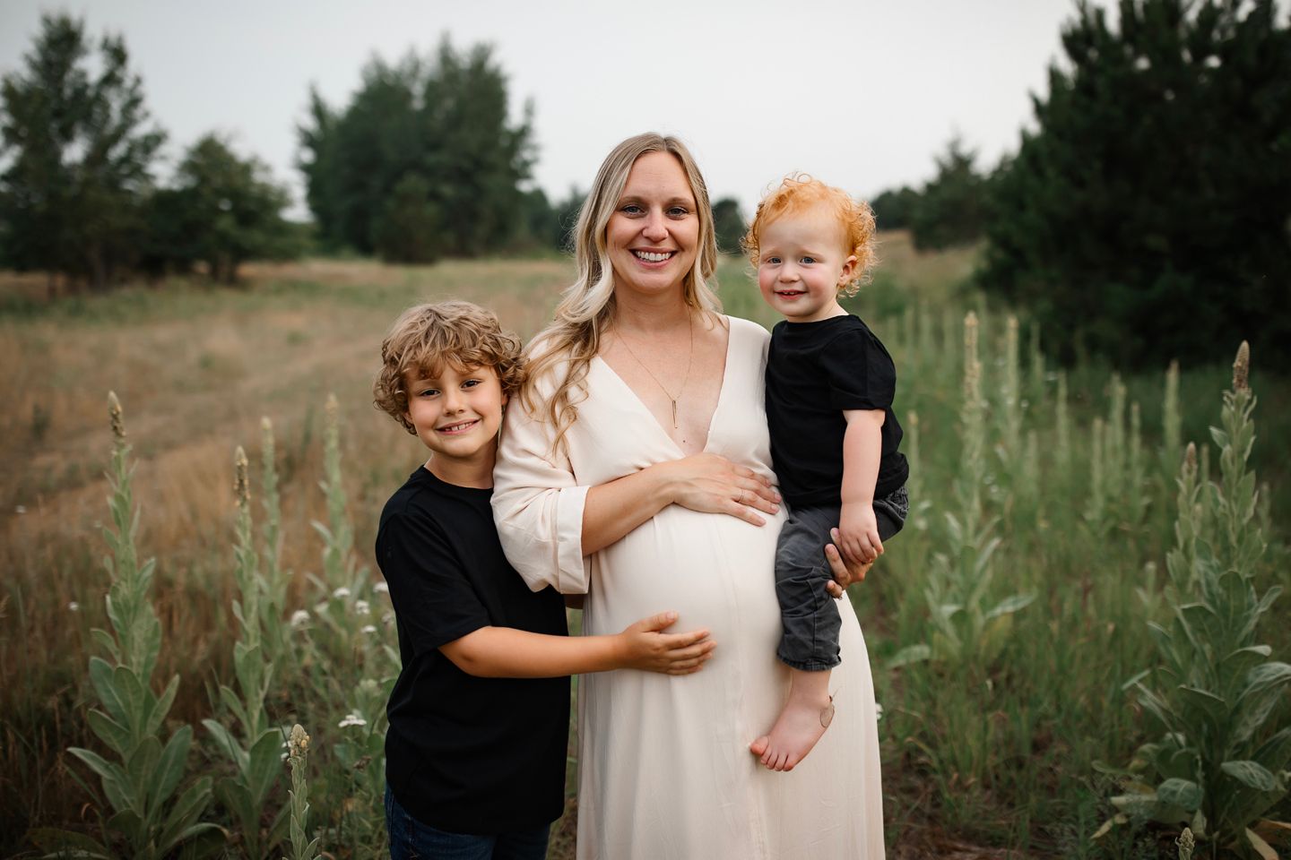 A maternity photo showing a family standing in a grassy field during golden hour.