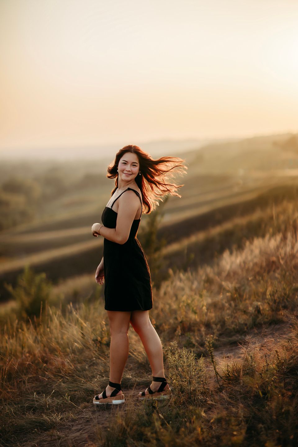 Person in a black dress twirling on a hilltop during golden hour with hair flowing in the wind.