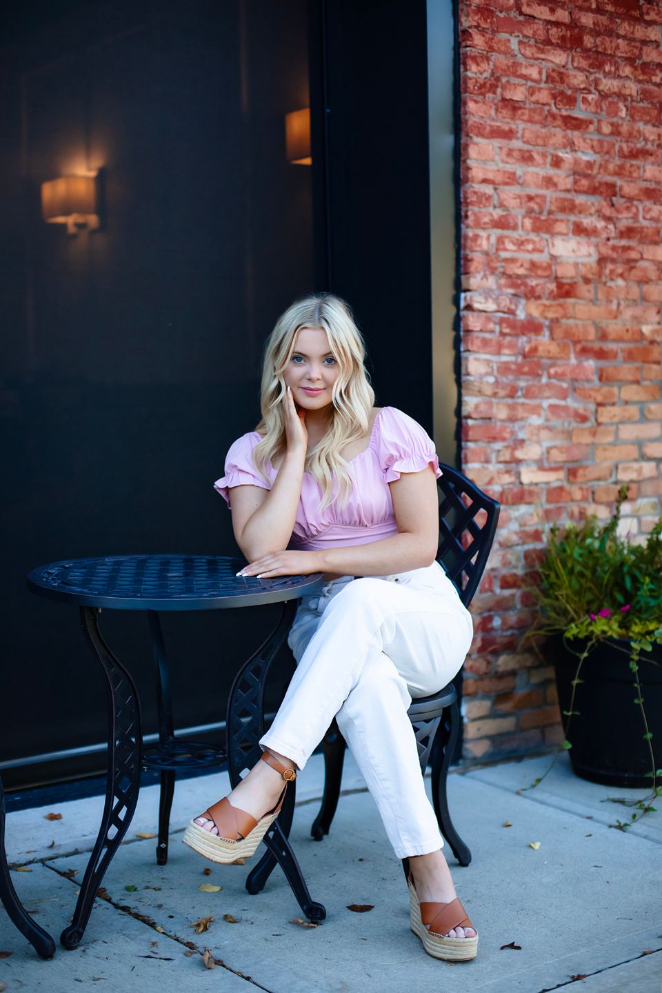 Lifestyle portrait at an outdoor cafe with brick wall background and bistro furniture.