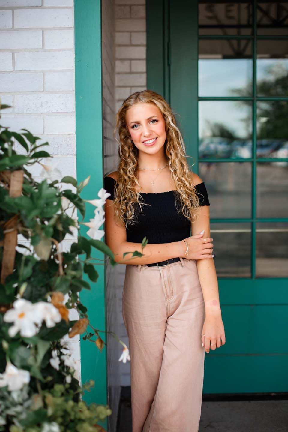 A stylish outfit featuring high-waisted beige pants and a black crop top against a white brick wall with green accents.
