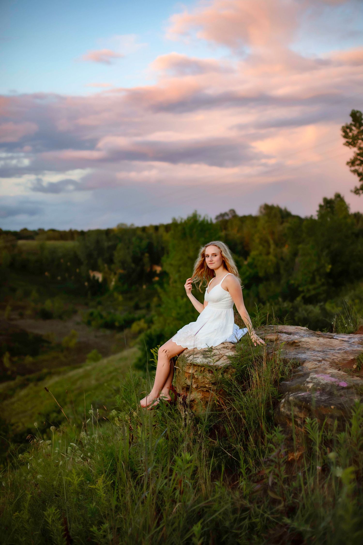 A dreamy outdoor portrait on a rocky outcrop during golden hour with pink clouds.
