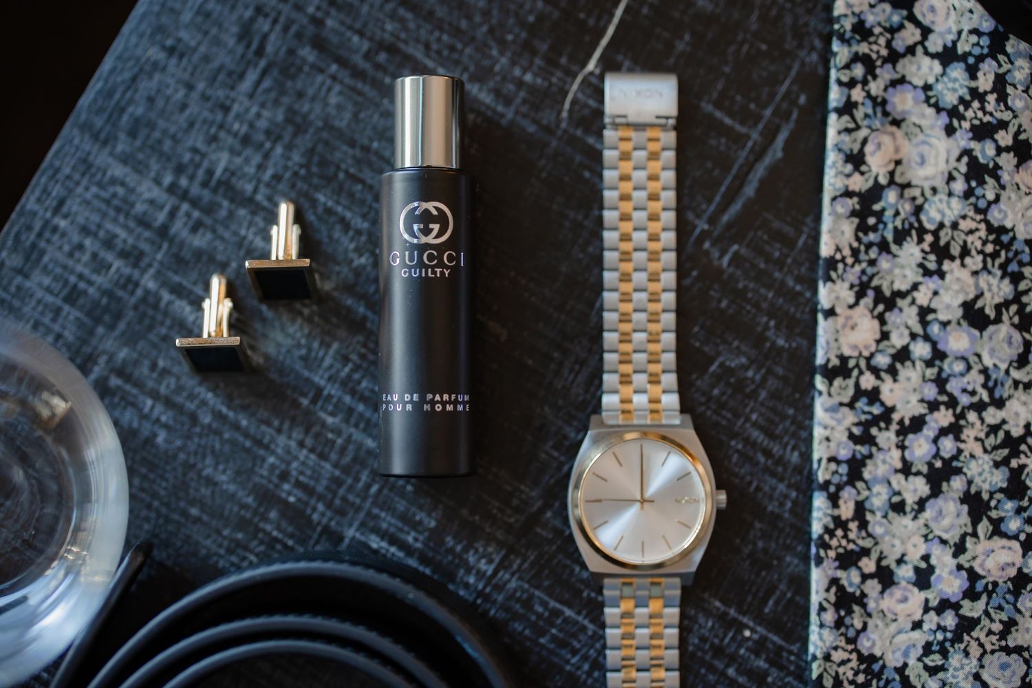 Wedding day accessories featuring a watch, cufflinks, perfume and patterned tie.