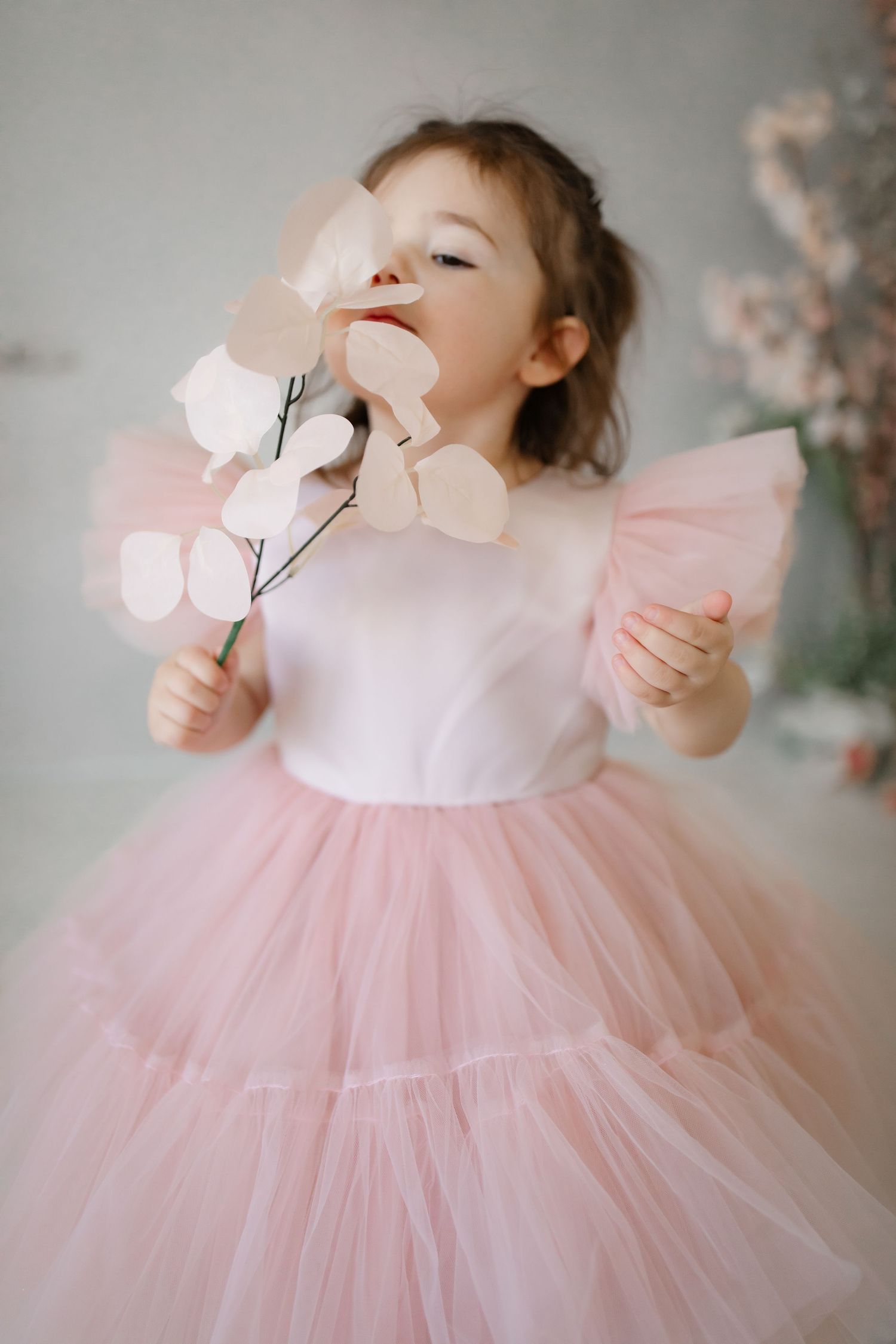 A dreamy portrait of a pink tulle dress with flutter sleeves and silk flowers against a soft background.
