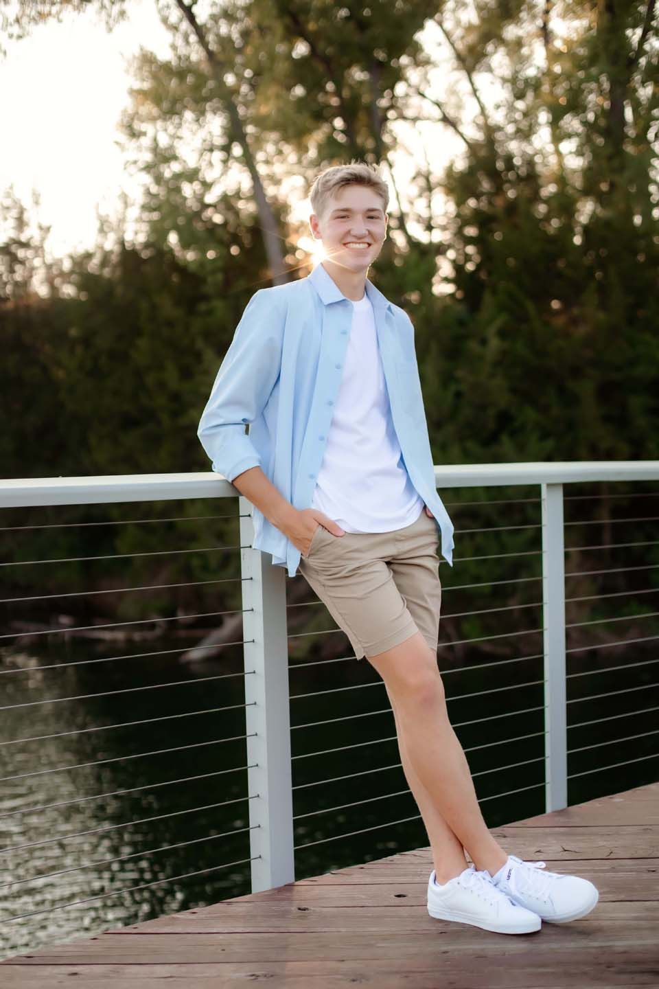 Sunset portrait on wooden dock wearing light blue shirt and khaki shorts.