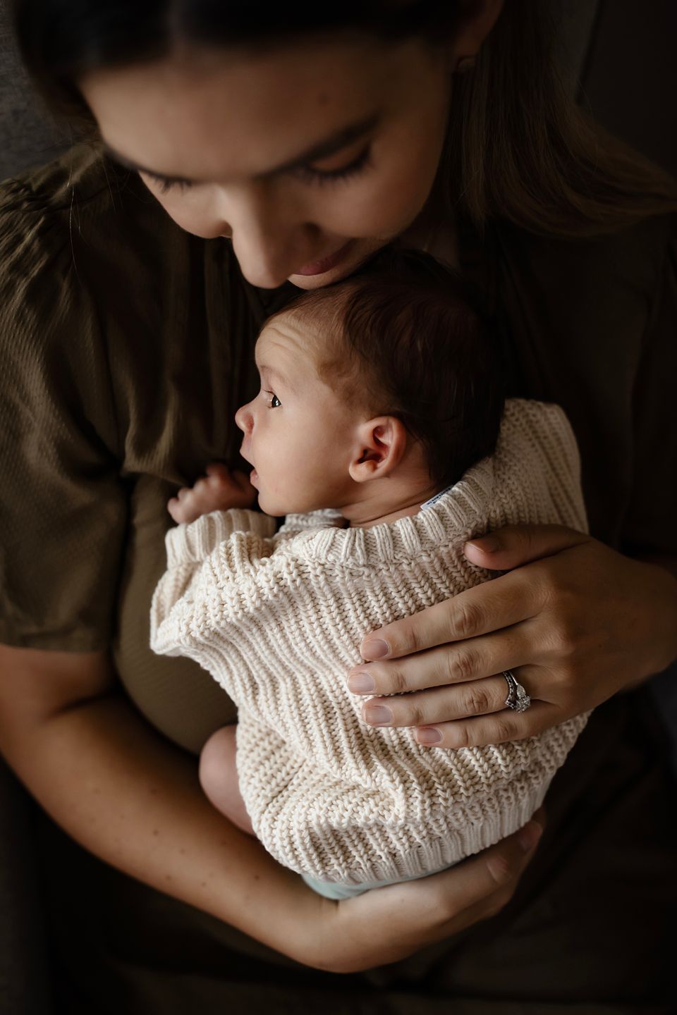 Tender moment between parent and baby wearing cozy cream knit sweater in moody lighting.
